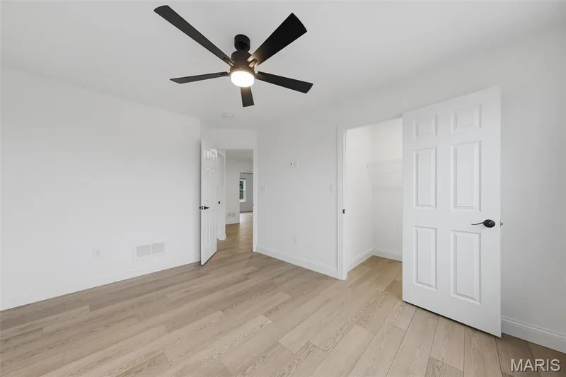 Wood-finish flooring, white paneled doors, ceiling fan with integrated lighting, and a built-in closet with shelving — 8 Shady Elm Court, St Charles, MO 63301