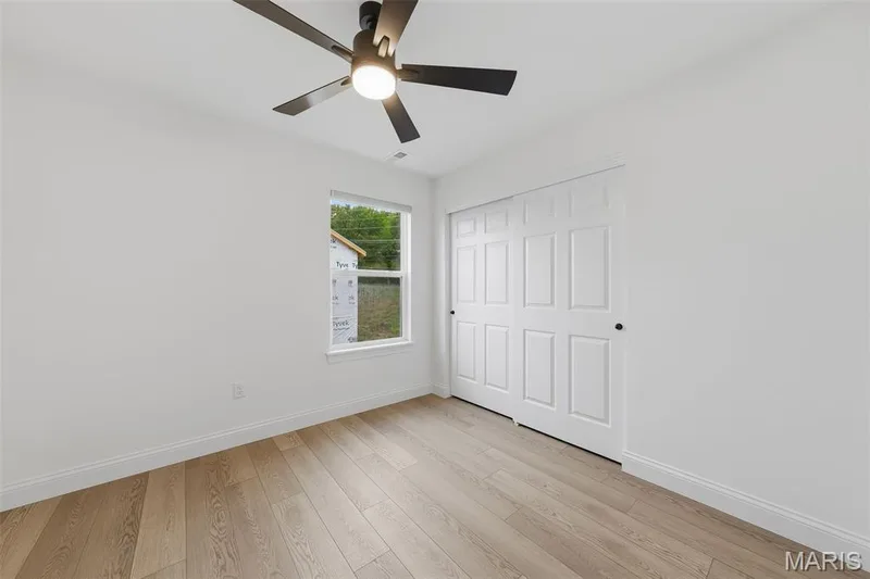 Light wood-finish flooring, white walls, modern ceiling fan with lighting, white trim, and white sliding closet doors — 8 Shady Elm Court, St Charles, MO 63301