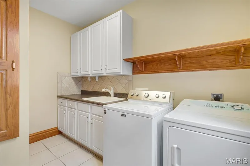 Thoughtfully designed for everyday functionality, the laundry room offers a built-in ironing board, sink, and generous storage space, including a separate closet area conveniently located around the corner. — 4030 Austin Drive, St Charles, MO 63304