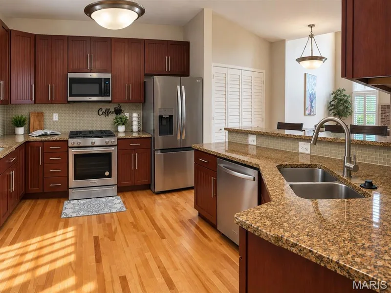 Kitchen featuring wood-finish flooring, rich wood cabinetry, stainless steel appliances, and stone-finish countertops with a tile backsplash — 3105 Wheeling Drive, St Charles, MO 63301