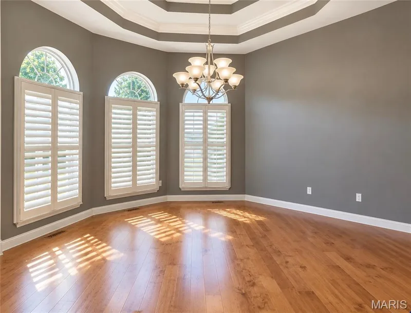 Tray ceiling with crown molding, wood-finish flooring, and arched windows featuring plantation shutters — 3105 Wheeling Drive, St Charles, MO 63301