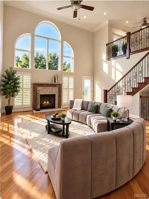 Two-story living area with arched windows, a stone-surround fireplace, wood-finish flooring, and a decorative wrought iron staircase — 3105 Wheeling Drive, St Charles, MO 63301