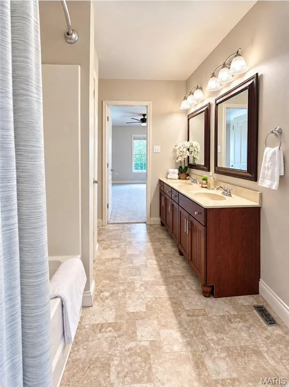 Bathroom featuring a double vanity with wood-finish cabinetry, dual framed mirrors, and a full bathtub with shower — 3105 Wheeling Drive, St Charles, MO 63301