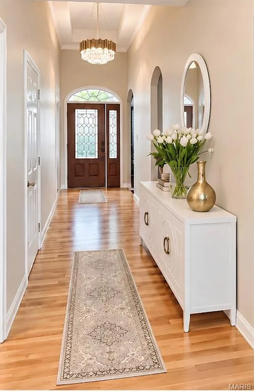 Foyer featuring wood-finish flooring, a coffered ceiling, a decorative chandelier, arched doorways, and a wood entry door with leaded glass panels — 3105 Wheeling Drive, St Charles, MO 63301
