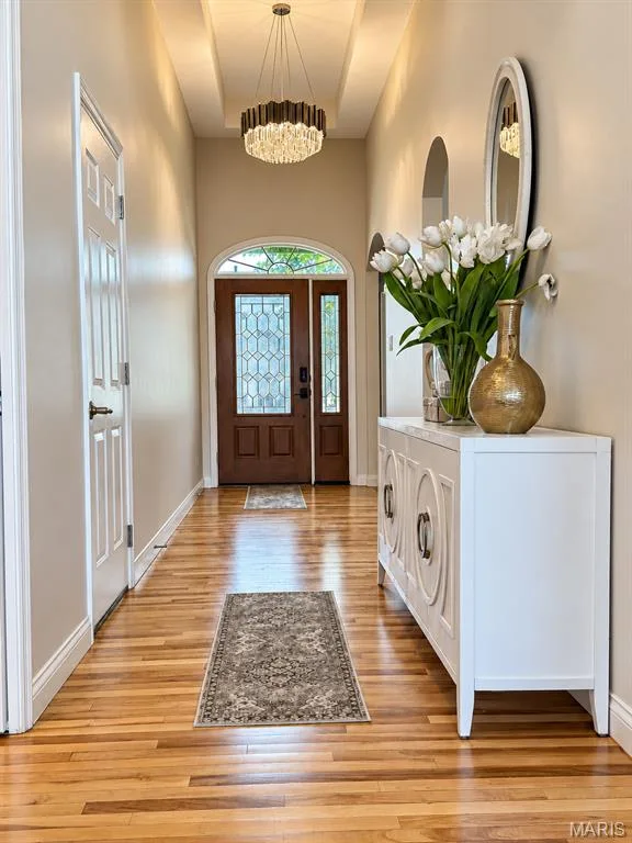 Foyer featuring wood-finish flooring, a coffered ceiling, a decorative chandelier, arched doorways, and a wood entry door with leaded glass panels — 3105 Wheeling Drive, St Charles, MO 63301