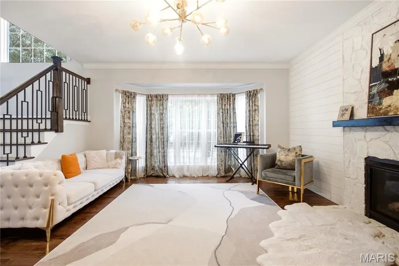 Hardwood flooring, bay window, stone fireplace with dark mantel, staircase with dark wood and wrought iron balusters, and a contemporary chandelier — 308 Graywynd Court, Lake St. Louis, MO 63367