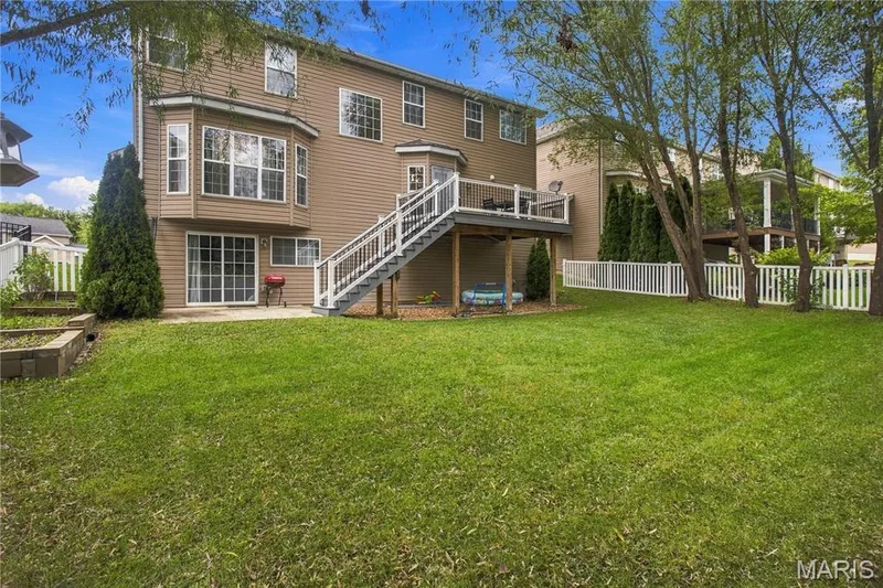 Expansive lawn with mature trees, a multi-level deck, a ground-level patio, and a bay window feature — 308 Graywynd Court, Lake St. Louis, MO 63367