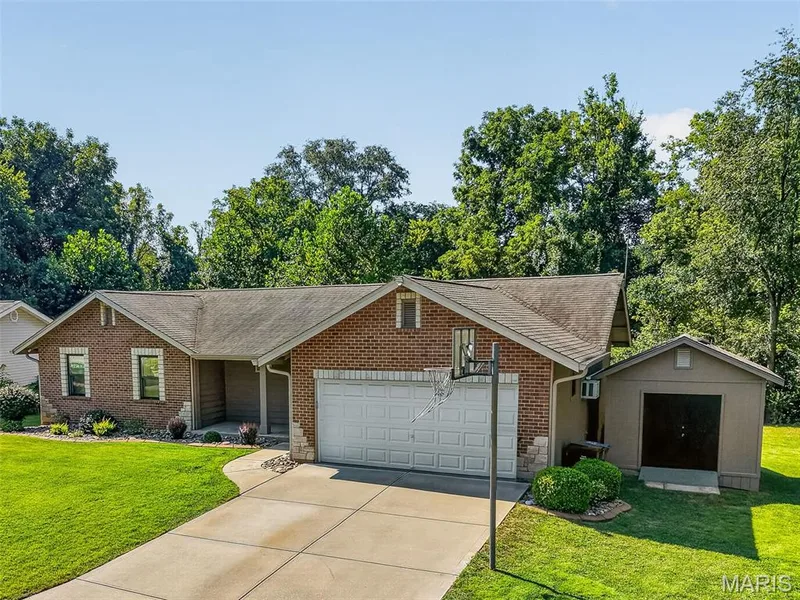 Brick-clad exterior with a covered entry, attached garage, concrete driveway, and a detached storage shed — 19 Novella Drive, St Peters, MO 63376