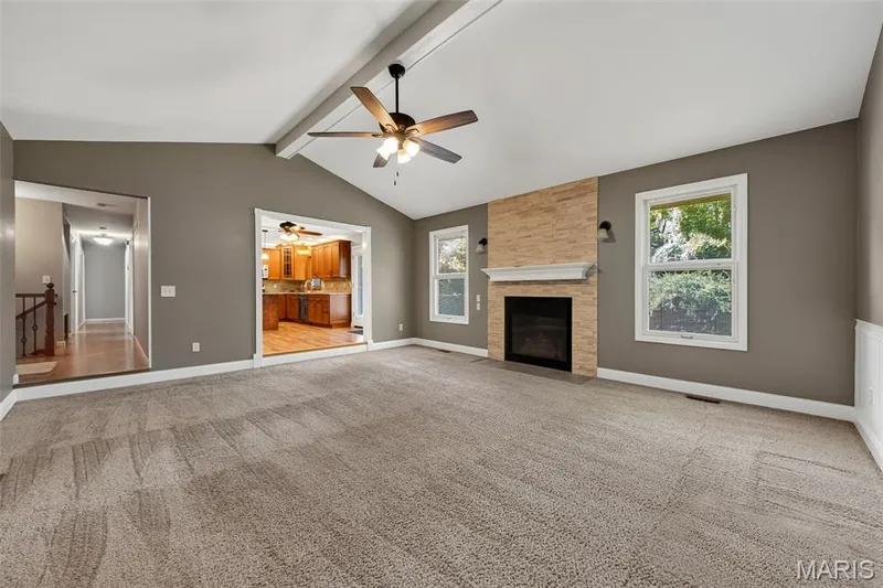 Vaulted ceiling with exposed beam, ceiling fan, carpet flooring, fireplace with stone surround and mantel, and multiple windows — 19 Novella Drive, St Peters, MO 63376