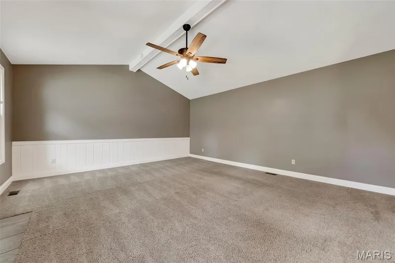 Spacious primary bedroom with vaulted ceiling, ceiling fan with integrated lighting, neutral taupe walls, white wainscoting accent, and soft carpet flooring throughout — 19 Novella Drive, St Peters, MO 63376