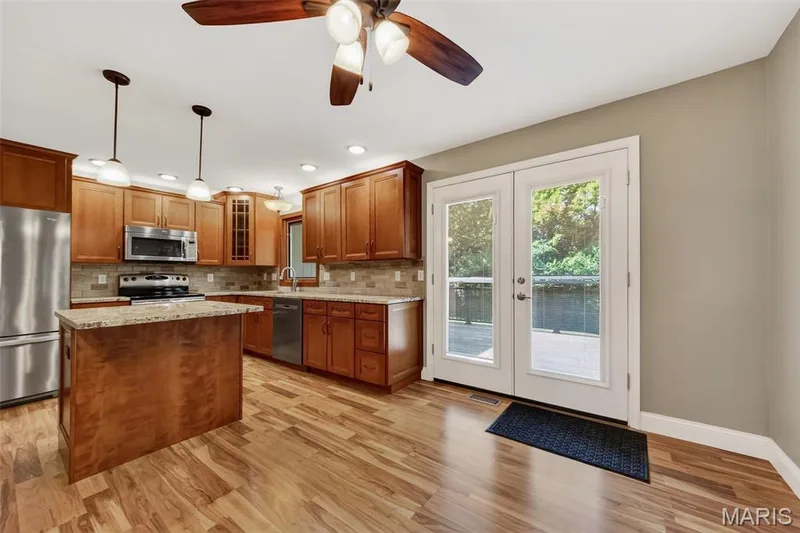 Wood-finish flooring, wood cabinetry, stainless steel appliances, granite-finish countertops, and double glass doors opening to a deck — 19 Novella Drive, St Peters, MO 63376