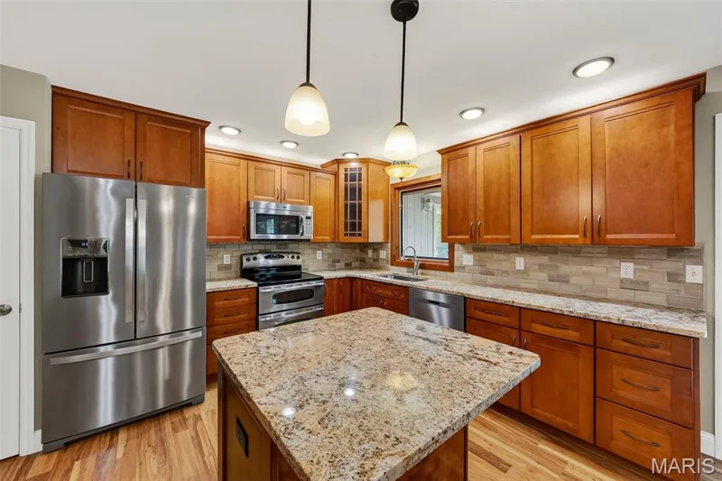 Kitchen featuring wood-finish flooring, recessed lighting, pendant lighting, built-in stainless steel appliances, and a central island with a granite countertop — 19 Novella Drive, St Peters, MO 63376