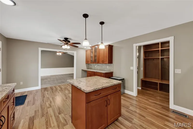 Wood-finish flooring throughout, presenting a kitchen island with stone countertop, accompanied by matching cabinetry — 19 Novella Drive, St Peters, MO 63376