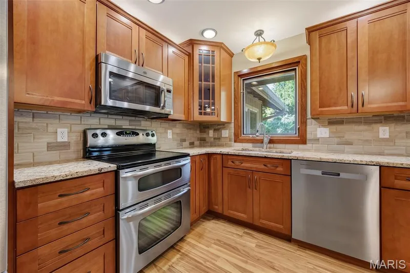 Wood-finish flooring, light wood cabinetry, stainless steel appliances, granite countertops, and a subway tile backsplash — 19 Novella Drive, St Peters, MO 63376
