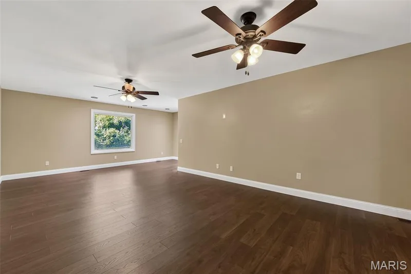 Spacious room featuring wood-finish flooring, neutral-toned walls, and multiple ceiling fans with integrated lighting — 19 Novella Drive, St Peters, MO 63376