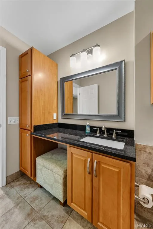 Vanity with black countertop and integrated sink, chrome faucet, wall-mounted lighting, and a framed mirror — 19 Novella Drive, St Peters, MO 63376
