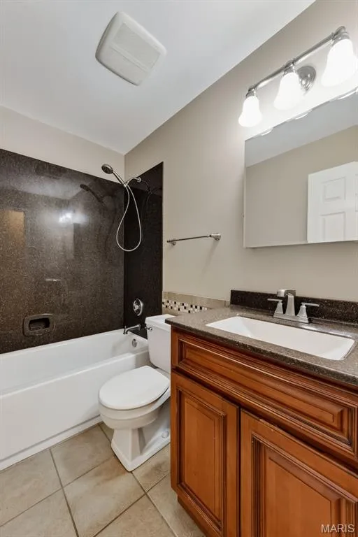 Bathroom featuring a white tub, shower with dark stone-finish surround, wood-finish vanity with an integrated sink, dark stone-finish countertop, and tile flooring — 19 Novella Drive, St Peters, MO 63376