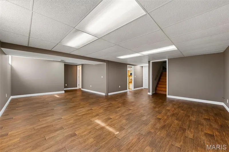 Expansive room featuring wood-look tile flooring, neutral wall tones, and recessed ceiling panels with integrated lighting — 19 Novella Drive, St Peters, MO 63376