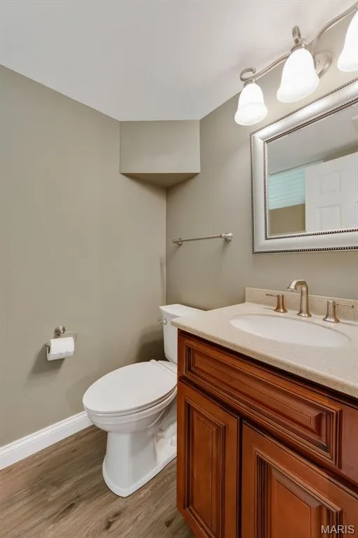 Elegant bathroom featuring warm wood-finish cabinetry with a ceramic countertop sink, brushed nickel fixtures, and framed mirror — 19 Novella Drive, St Peters, MO 63376
