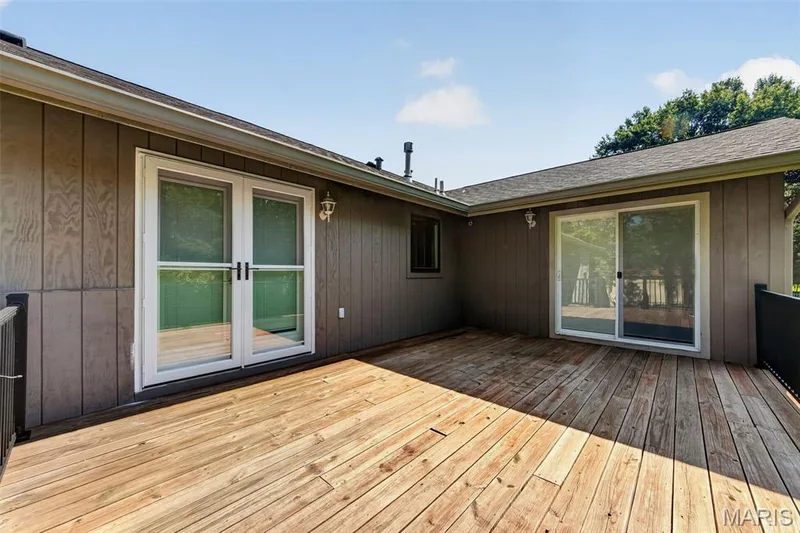 Expansive wood deck with two sets of sliding glass doors, a wall-mounted exterior light fixture, and black metal railings — 19 Novella Drive, St Peters, MO 63376