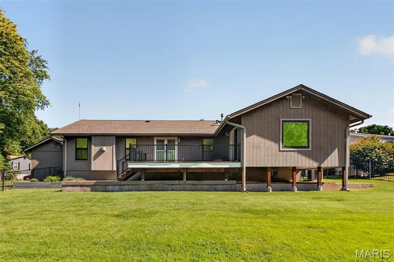 Expansive backyard featuring a manicured lawn, multi-level deck with black railings, and a gravel-covered lower patio area — 19 Novella Drive, St Peters, MO 63376