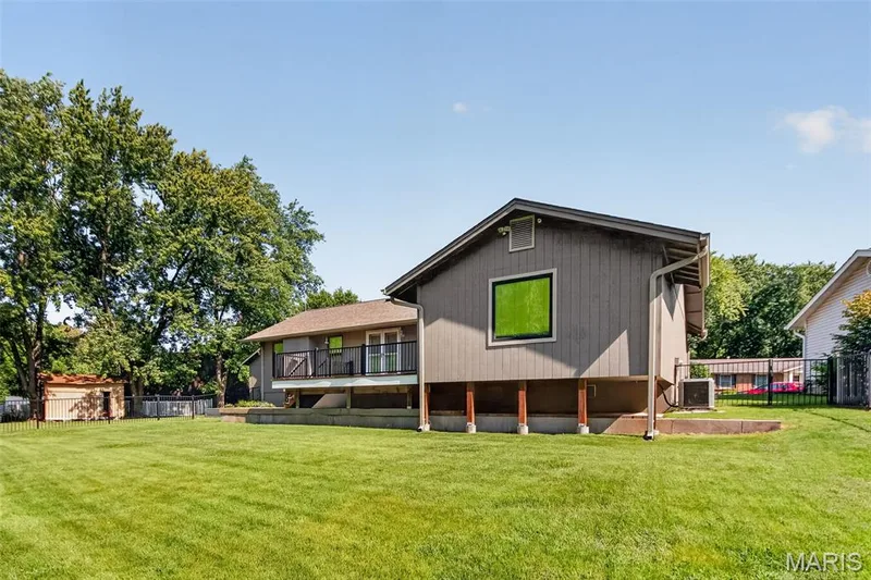 Expansive green lawn, elevated deck with black railing, attached storage shed, and mature trees — 19 Novella Drive, St Peters, MO 63376