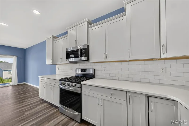 White shaker-style cabinetry, stainless steel range, built-in microwave, subway tile backsplash, and wood-finish flooring — 622 Cruden Bay Court, Dardenne Prairie, MO 63368