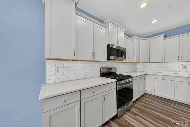 Kitchen featuring white shaker cabinetry, white countertops, subway tile backsplash, stainless steel gas range, and wood-finish flooring — 622 Cruden Bay Court, Dardenne Prairie, MO 63368