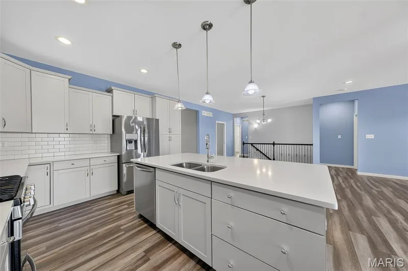 Kitchen featuring a large island with an integrated sink, pendant lighting, stainless steel appliances, light gray cabinetry, and wood-finish flooring — 622 Cruden Bay Court, Dardenne Prairie, MO 63368