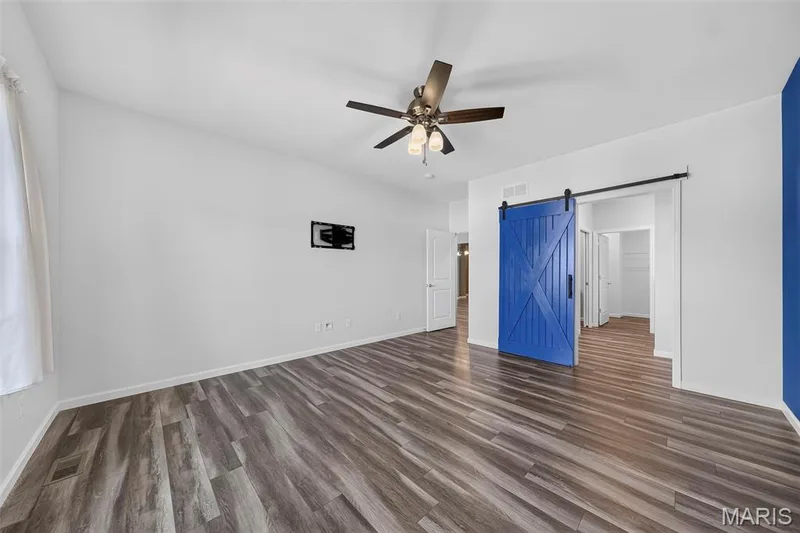 Wood-finish flooring, vaulted ceiling, ceiling fan with integrated lighting, and a blue barn door with black hardware — 622 Cruden Bay Court, Dardenne Prairie, MO 63368