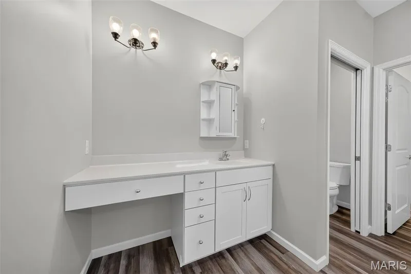 White vanity with integrated sink, white countertop, wood-finish flooring, and wall-mounted light fixtures — 622 Cruden Bay Court, Dardenne Prairie, MO 63368