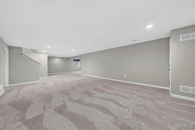 Expansive carpeted area with recessed lighting, light gray walls, and a stairway featuring a dark handrail — 622 Cruden Bay Court, Dardenne Prairie, MO 63368