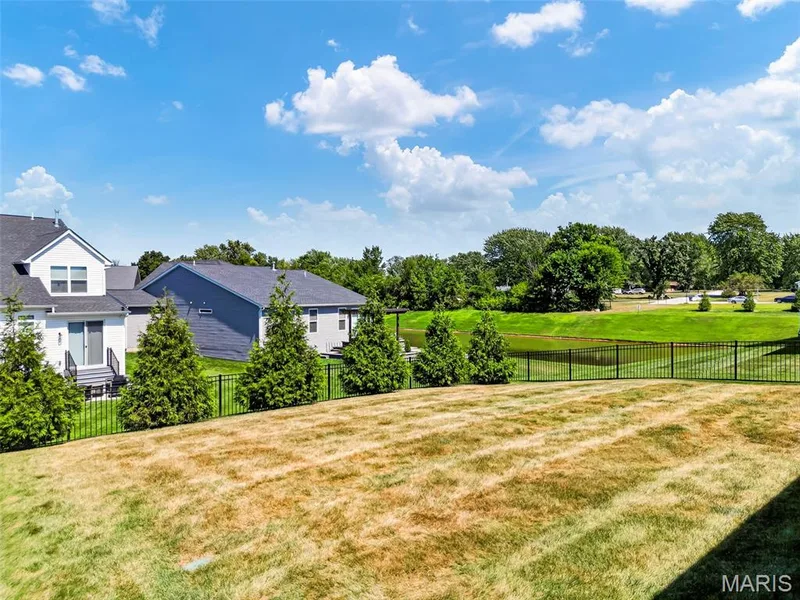 Expansive backyard featuring a black metal fence, evergreen plantings, and a water feature — 622 Cruden Bay Court, Dardenne Prairie, MO 63368