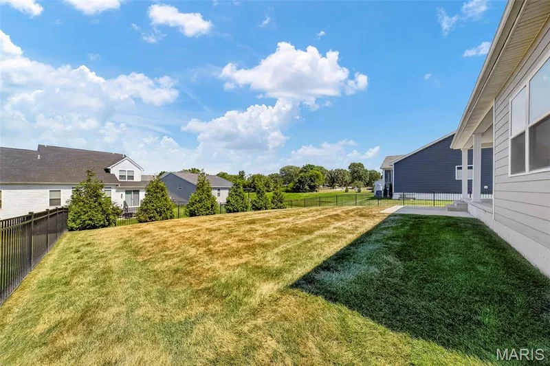 Expansive backyard featuring a partial patio, a black metal fence, and mature landscaping — 622 Cruden Bay Court, Dardenne Prairie, MO 63368