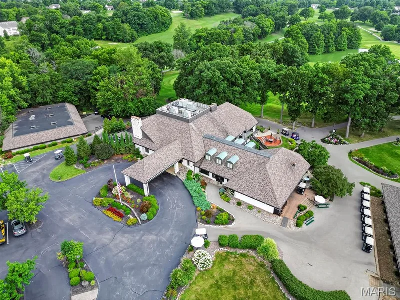 Expansive property featuring a large main building with multiple rooflines, extensive paved driveways, a landscaped entrance with a flag pole, and surrounding mature trees — 622 Cruden Bay Court, Dardenne Prairie, MO 63368