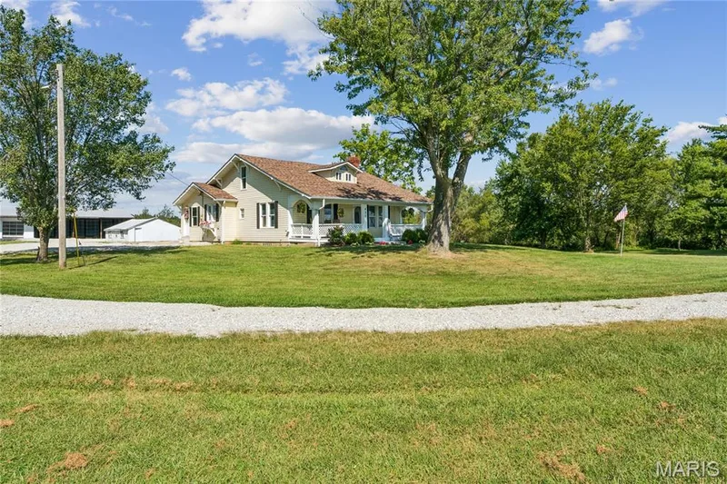 Expansive gravel driveway leading to a residence featuring a covered porch, multiple windows with dark shutters, and a prominent gable roof — 435 Highway T, Foristell, MO 63348