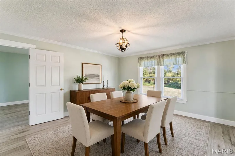 Elegant dining room featuring a wood-finish dining table, upholstered dining chairs, wood-finish cabinetry, large windows with natural light, and hardwood-style flooring throughout the space — 435 Highway T, Foristell, MO 63348