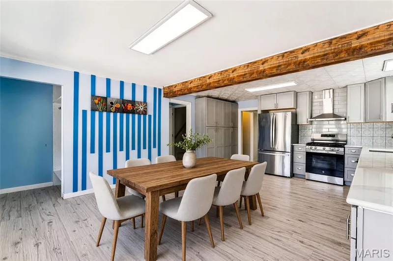 Open-concept dining area featuring wood-finish flooring, exposed wood beam, recessed lighting, and built-in kitchen cabinetry with stainless steel appliances — 435 Highway T, Foristell, MO 63348