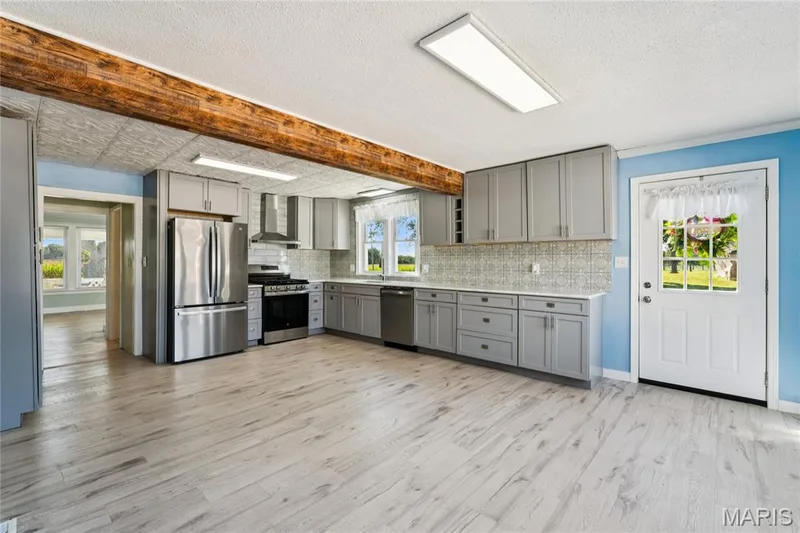 Kitchen featuring wood-finish flooring, gray cabinetry, stainless steel appliances, and a tiled backsplash — 435 Highway T, Foristell, MO 63348
