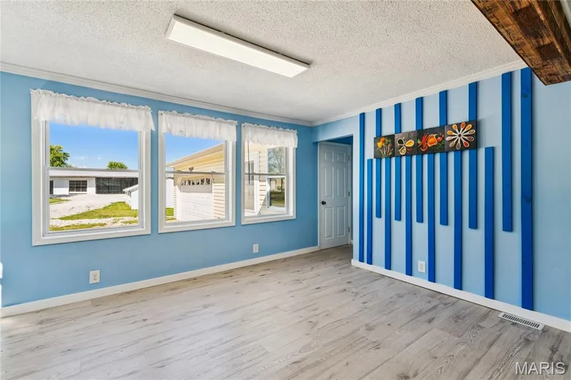 Light wood-finish flooring, three windows with white trim, a decorative blue accent wall, and a white interior door — 435 Highway T, Foristell, MO 63348