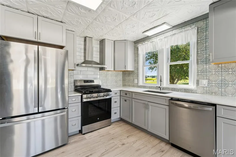 Stainless steel appliances, light gray cabinetry, patterned tile backsplash, wood-finish flooring, and white countertops — 435 Highway T, Foristell, MO 63348