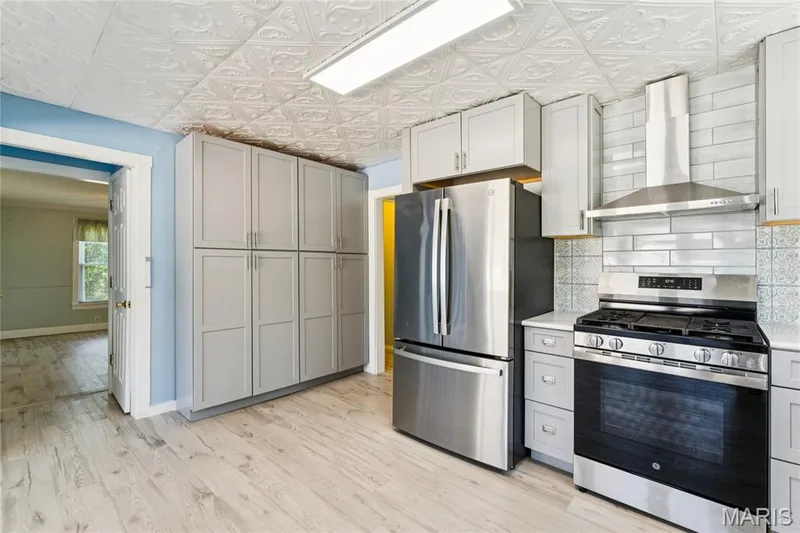 Modern kitchen featuring stainless steel appliances, light gray cabinetry, wood-finish flooring, a patterned ceiling, and subway tile backsplash — 435 Highway T, Foristell, MO 63348