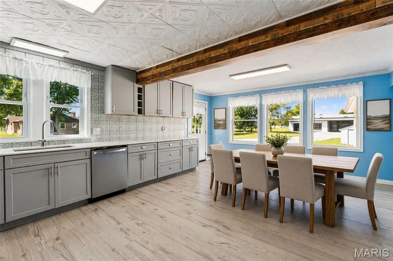 Open-concept kitchen and dining area featuring custom gray cabinetry with stainless steel appliances, subway tile backsplash, and wood-finish flooring throughout — 435 Highway T, Foristell, MO 63348