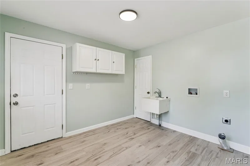 Wood-finish flooring, white overhead cabinetry, utility sink with chrome faucet, and flush mount ceiling lighting — 435 Highway T, Foristell, MO 63348