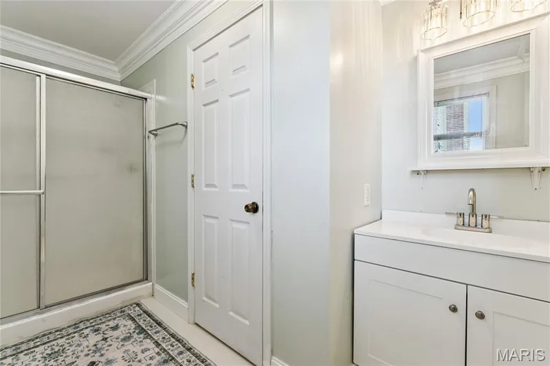 Spa-inspired primary bathroom featuring a frameless glass shower enclosure with geometric tile flooring, a white vanity with dual-handle faucet and ample countertop space, recessed medicine cabinet with mirror, and crisp white cabinetry throughout — 435 Highway T, Foristell, MO 63348