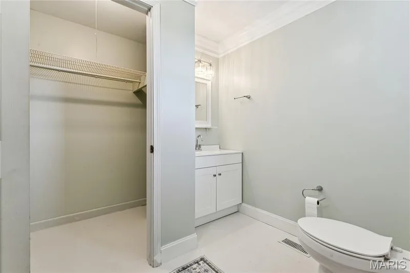 Bright and functional bathroom featuring a white vanity with ample storage, ceramic tile flooring, a toilet with elongated bowl, and a spacious walk-in closet with shelving and hanging rod for organized storage — 435 Highway T, Foristell, MO 63348