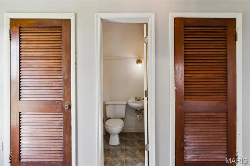 White toilet with a wall-mounted sink, ceramic tile flooring, and a wall-mounted light fixture — 435 Highway T, Foristell, MO 63348
