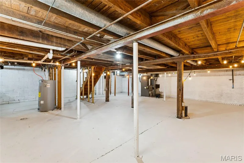 Expansive unfinished basement featuring a concrete floor, exposed wood ceiling beams, painted block walls, and a visible water heater — 435 Highway T, Foristell, MO 63348