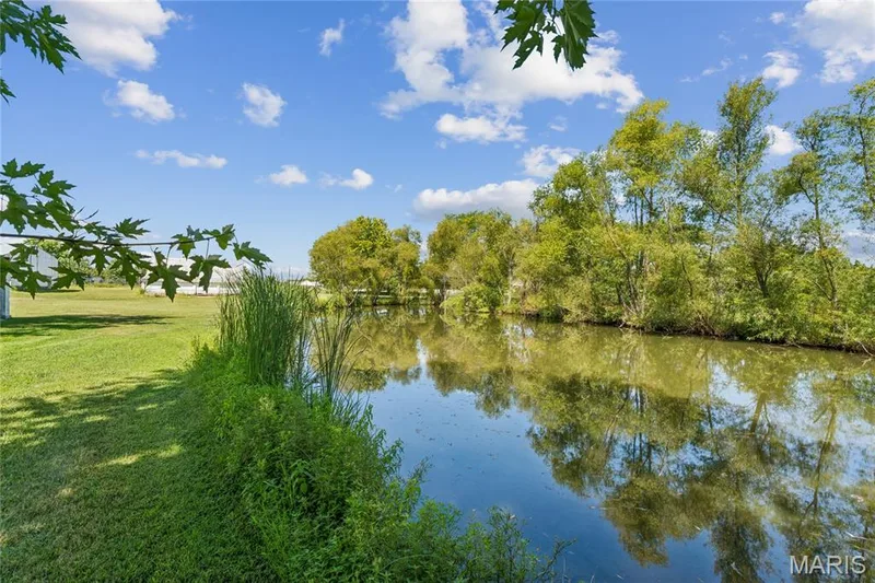 Expansive green lawn bordering a natural water feature with reflective surfaces and mature trees — 435 Highway T, Foristell, MO 63348