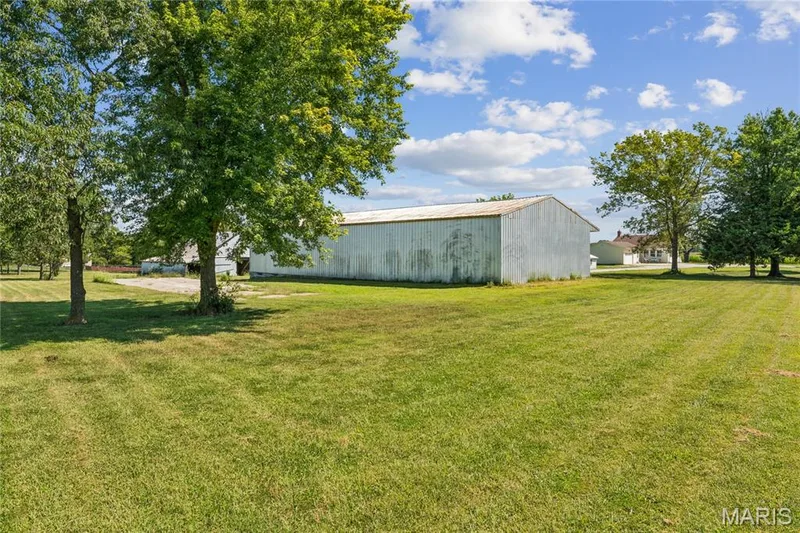 Expansive green lawn with mature trees and a large outbuilding with a metal roof — 435 Highway T, Foristell, MO 63348